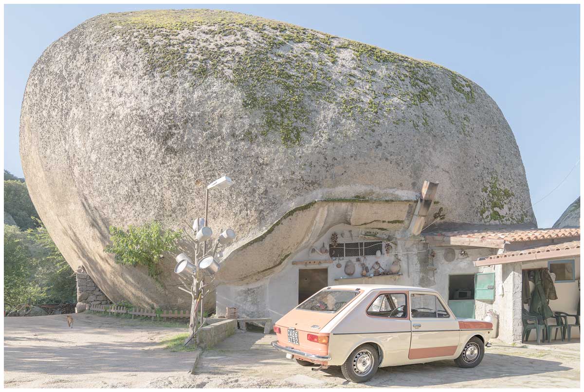 fotografia di una piccola auto parcheggiata davanti a una grande roccia.